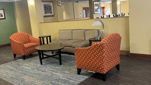 Um hall com um sofá, duas poltronas estampadas, uma mesa pequena e um abajur.