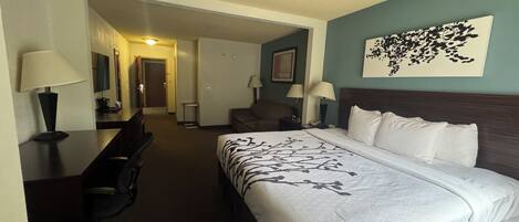 A hotel room with a bed, desk, chair, and a painting on the wall.