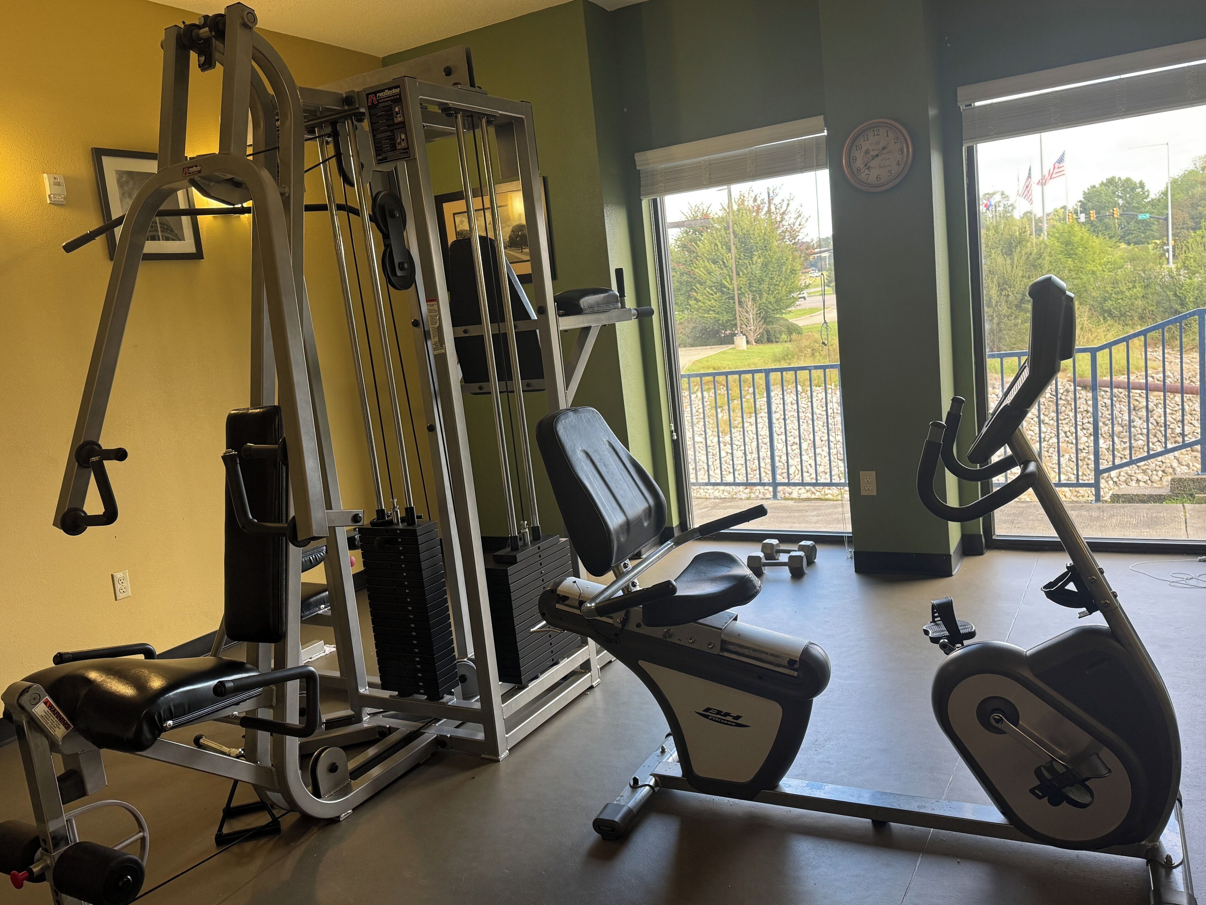 A gym with exercise equipment, a bench, and a window with a view of a park.