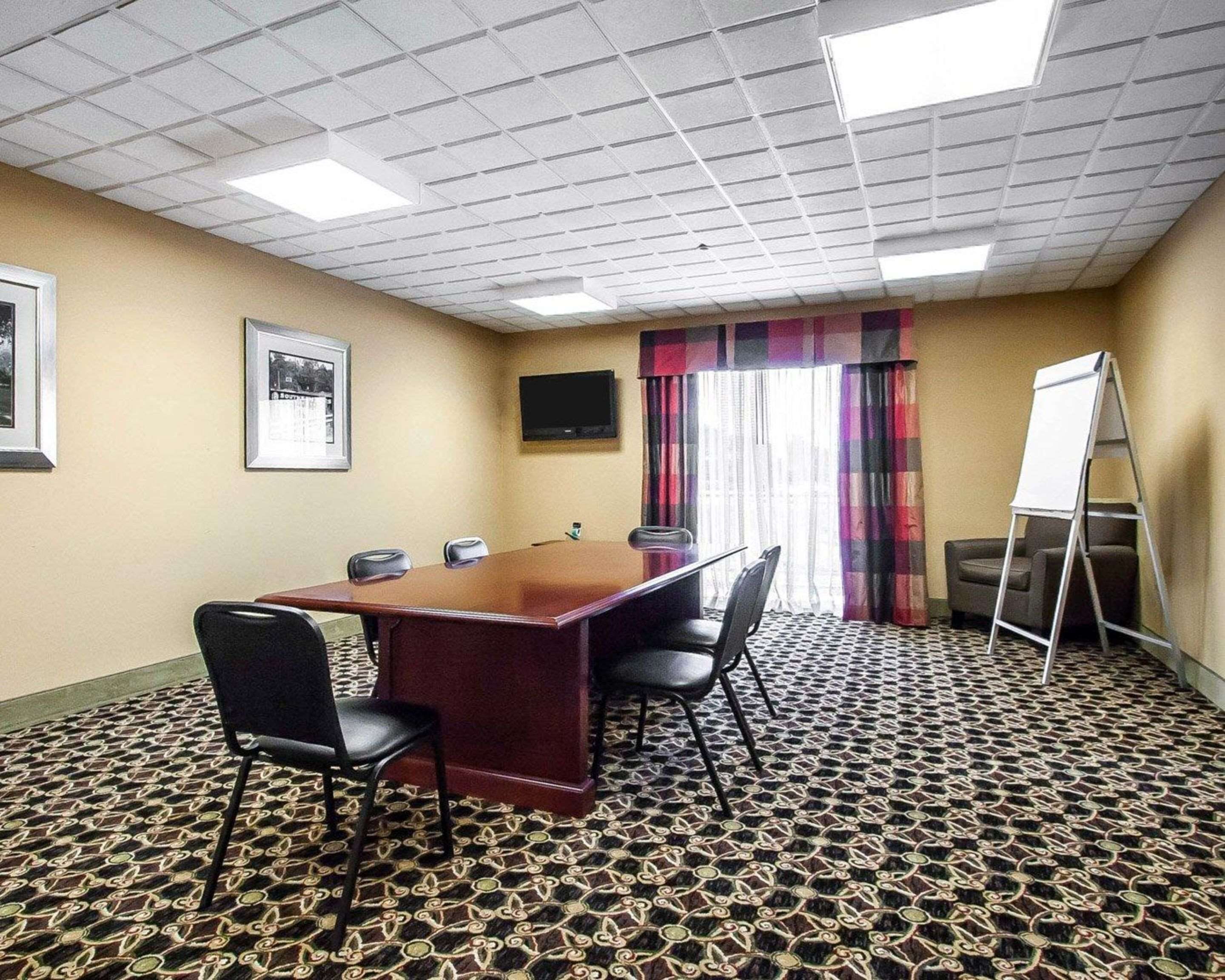 A conference room with a long table, four chairs, a whiteboard, and a patterned carpet.