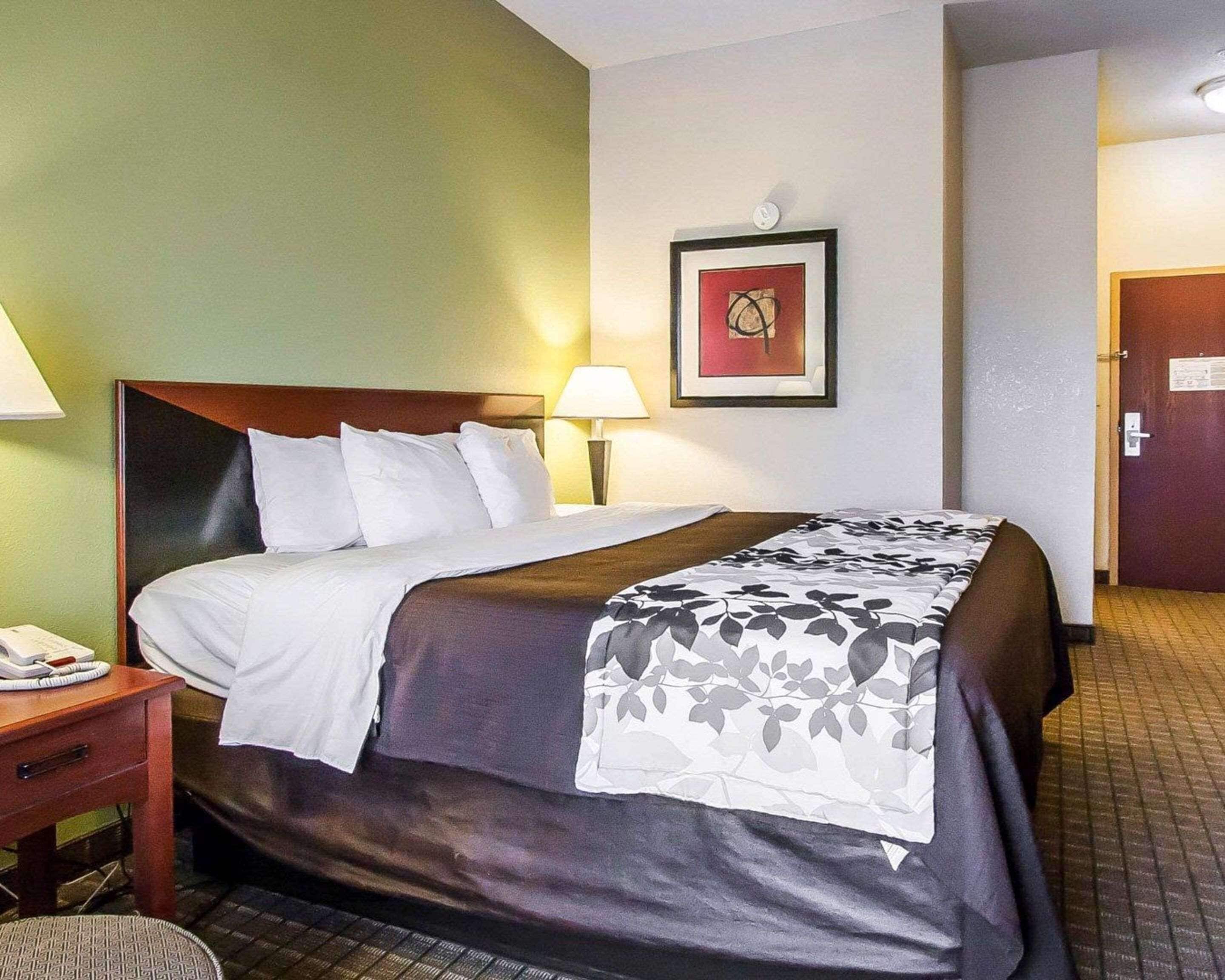 A hotel room with a bed, bedside table, lamp, and a framed picture on the wall.