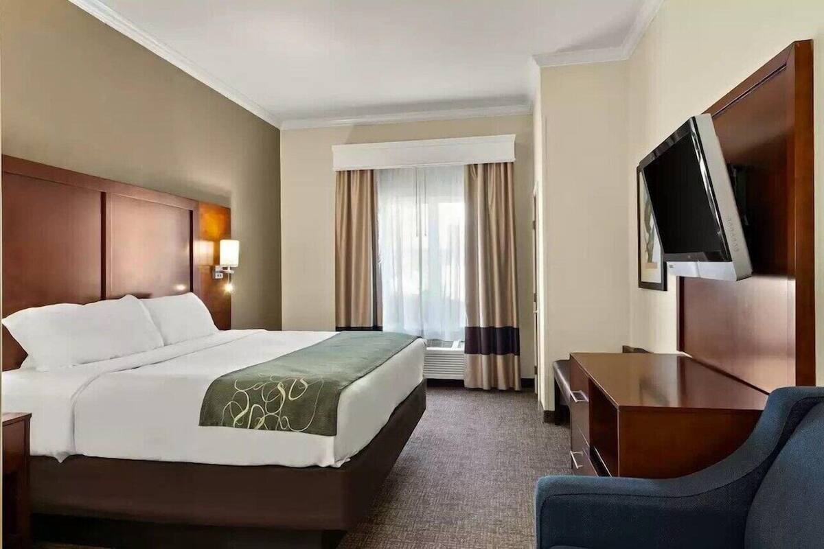 A hotel room with a bed, a desk, a chair, a TV, and a window with curtains.