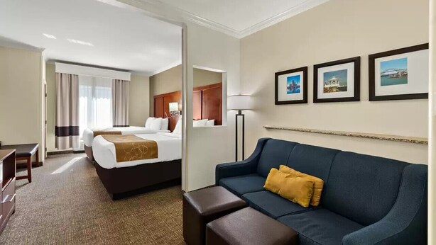 A hotel room with a bed, a sofa, a desk, and a lamp. There are framed pictures on the wall. - Comfort Suites Corpus Christi Central (Corpus Christi)