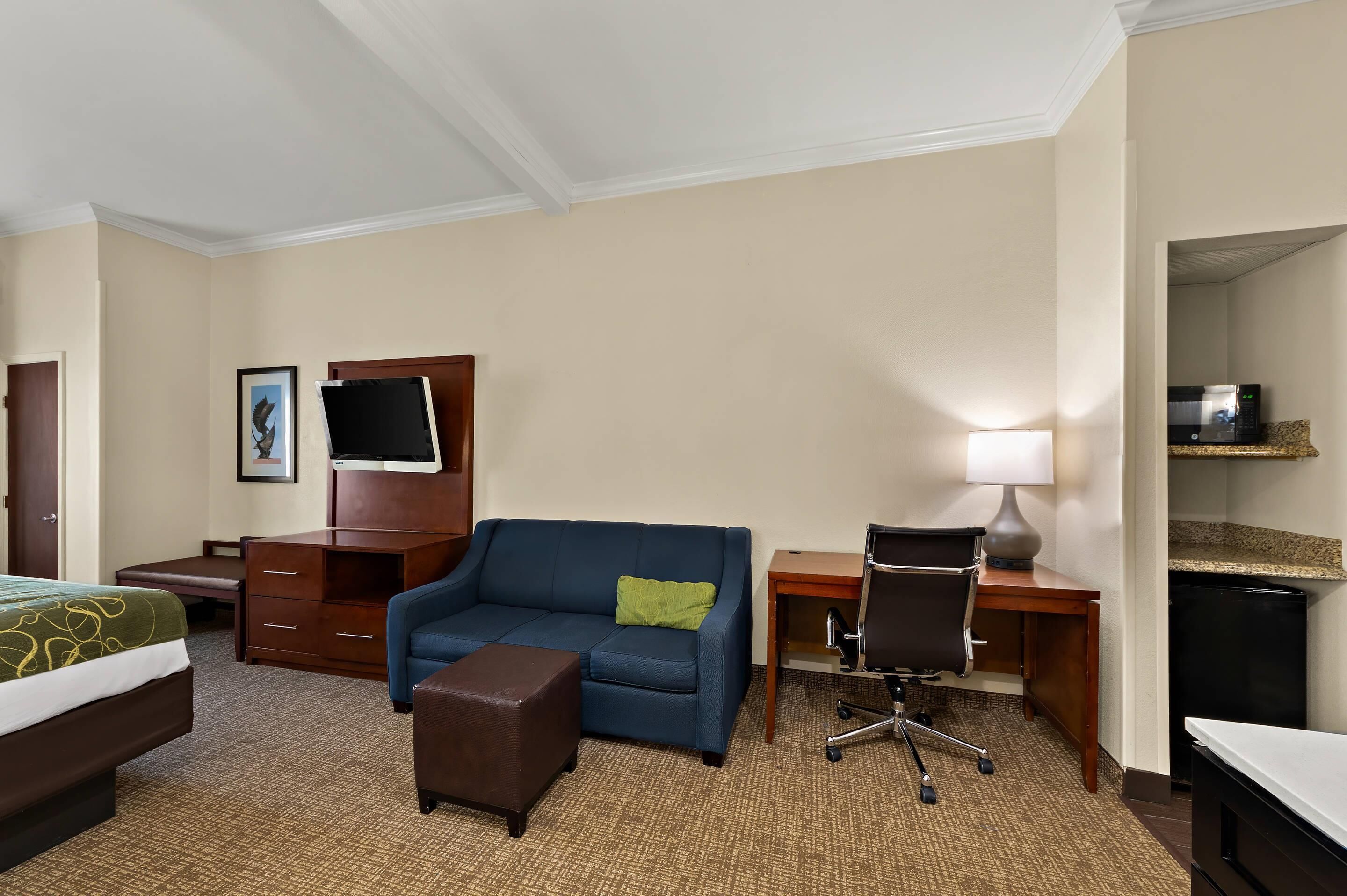 A hotel room with a bed, a blue sofa, a desk with a lamp, a chair, and a TV on a wooden cabinet.