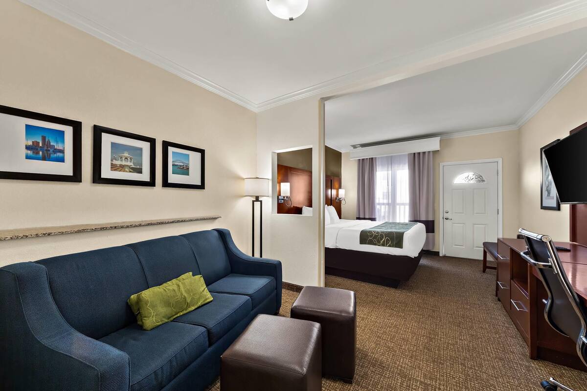 A hotel room with a blue sofa, a bed, a desk, and a television.