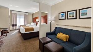 A hotel room with a bed, a sofa, a desk, and a lamp. There are three framed pictures on the wall. - Comfort Suites Corpus Christi Central (Corpus Christi)