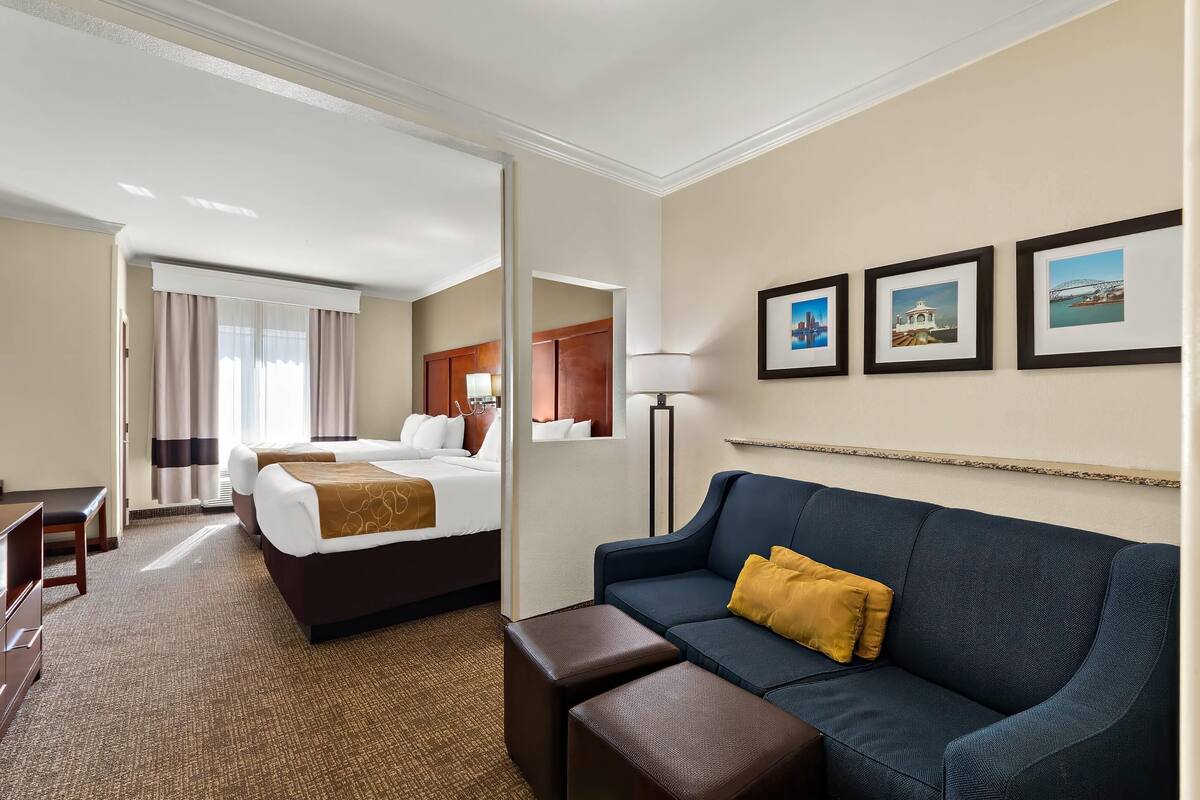 A hotel room with a bed, a sofa, a desk, and a lamp. There are three framed pictures on the wall.