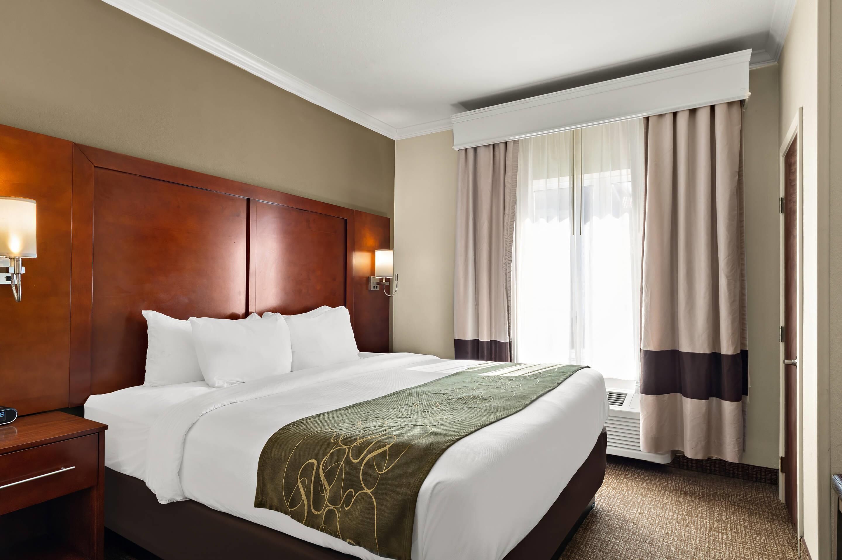Habitación de hotel con una cama grande, cabecera de madera, lámparas de noche, una ventana con cortinas y un equipo de aire acondicionado.