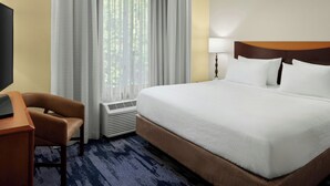 A hotel room with a large bed, a desk, a chair, a window with curtains, and a wall-mounted lamp. - Fairfield Inn & Suites by Marriott Carlisle (Carlisle)