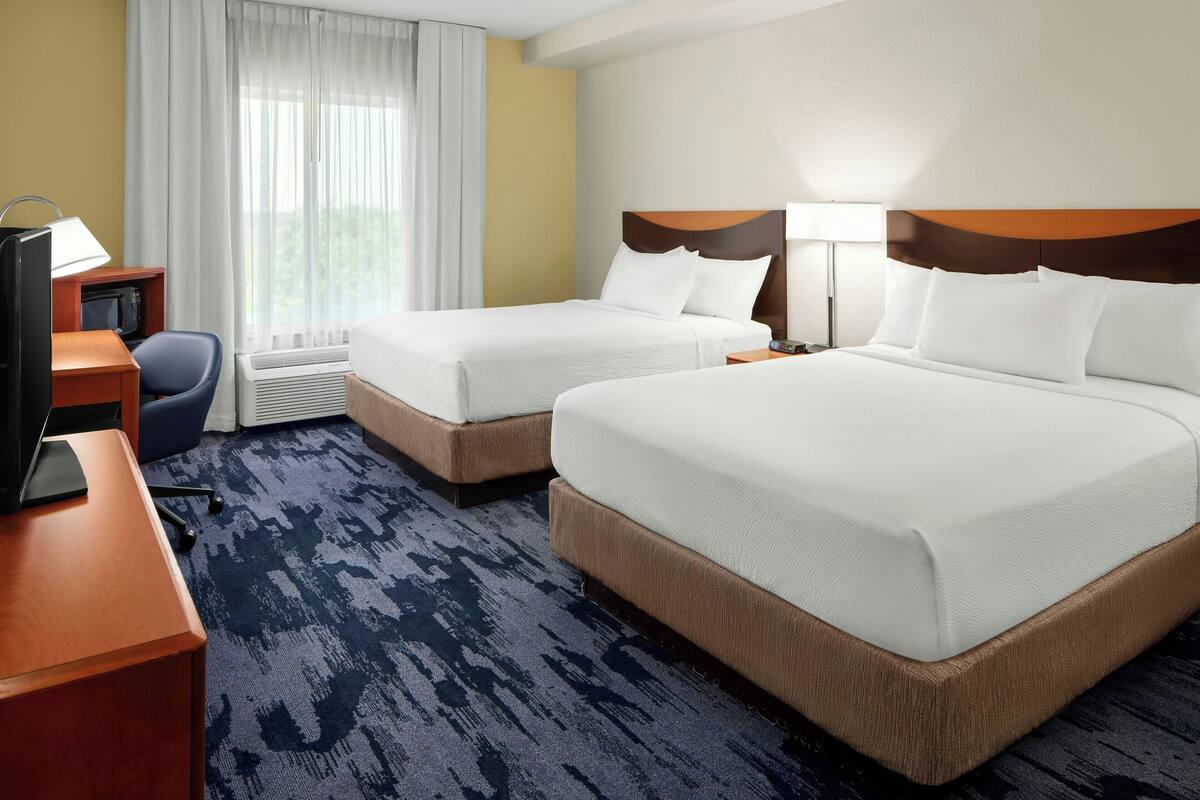 A hotel room with two beds, a desk with a computer, a chair, and a window with curtains.