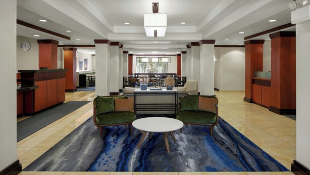 A lobby with a reception desk, seating area with a round table, and a bar in the background. - Fairfield Inn & Suites by Marriott Carlisle (Carlisle)