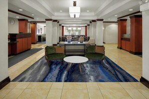 A lobby with a reception desk, seating area with a round table, and a bar in the background. - Fairfield Inn & Suites by Marriott Carlisle (Carlisle)