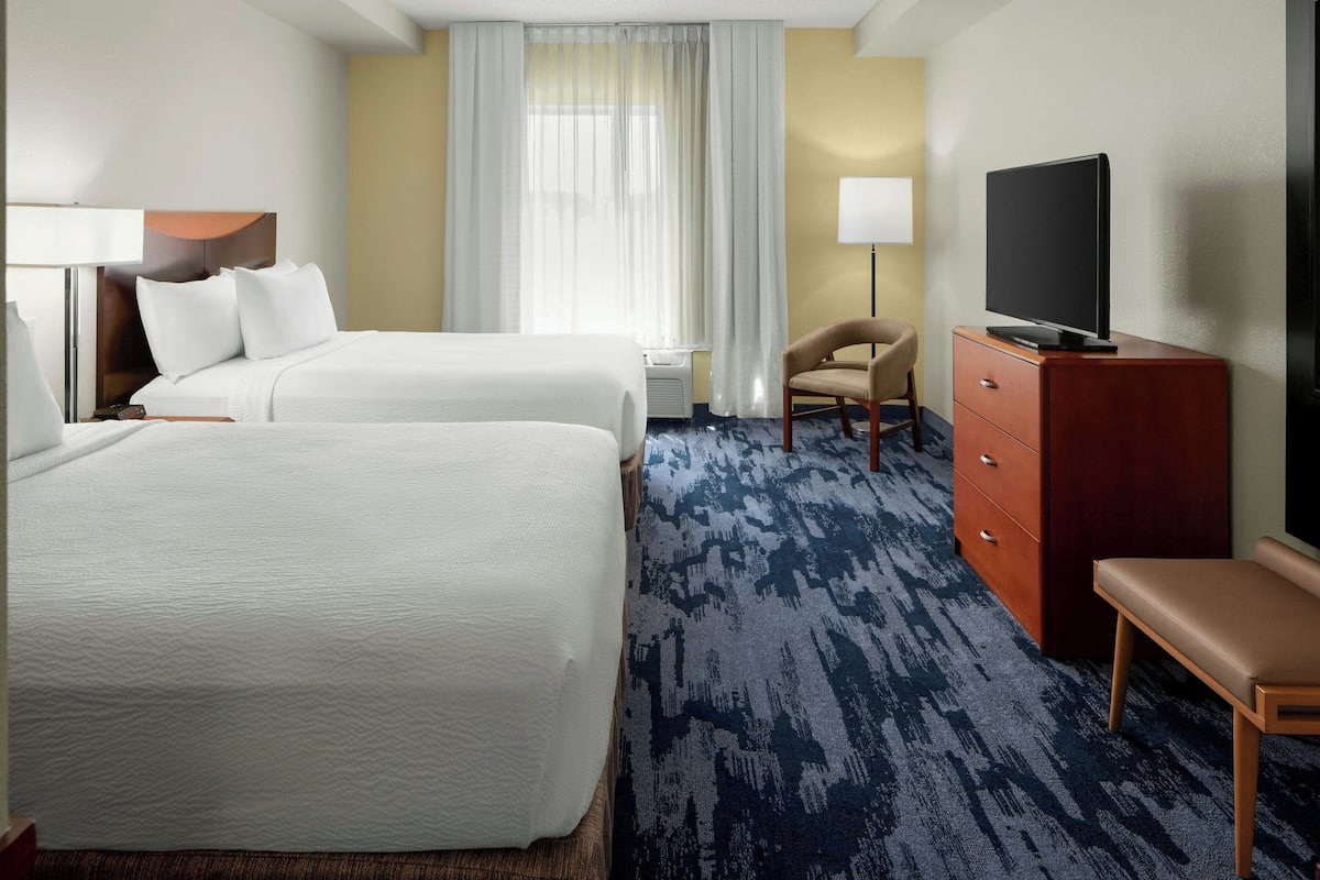 A hotel room with two beds, a TV, a desk, and a chair.