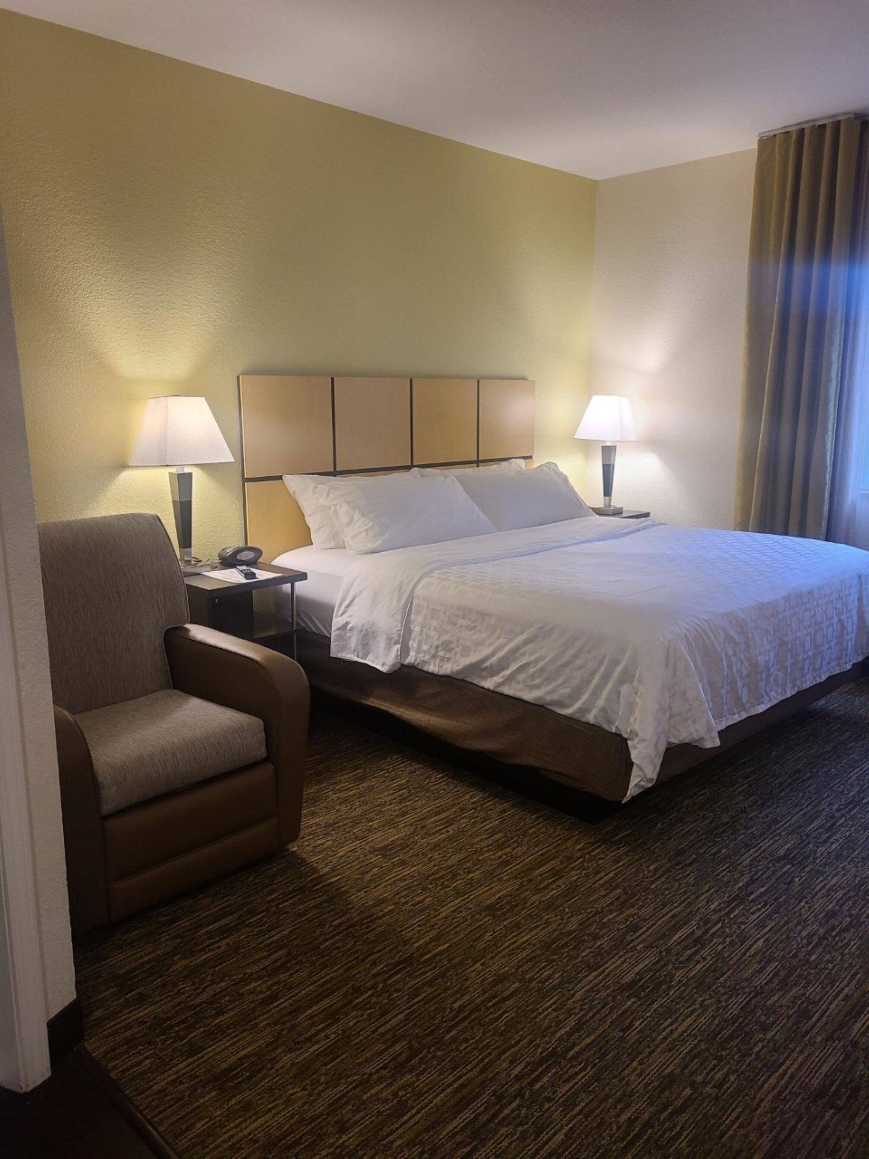 Habitación de hotel con cama, dos lámparas de noche, una silla y mesita de noche con teléfono.