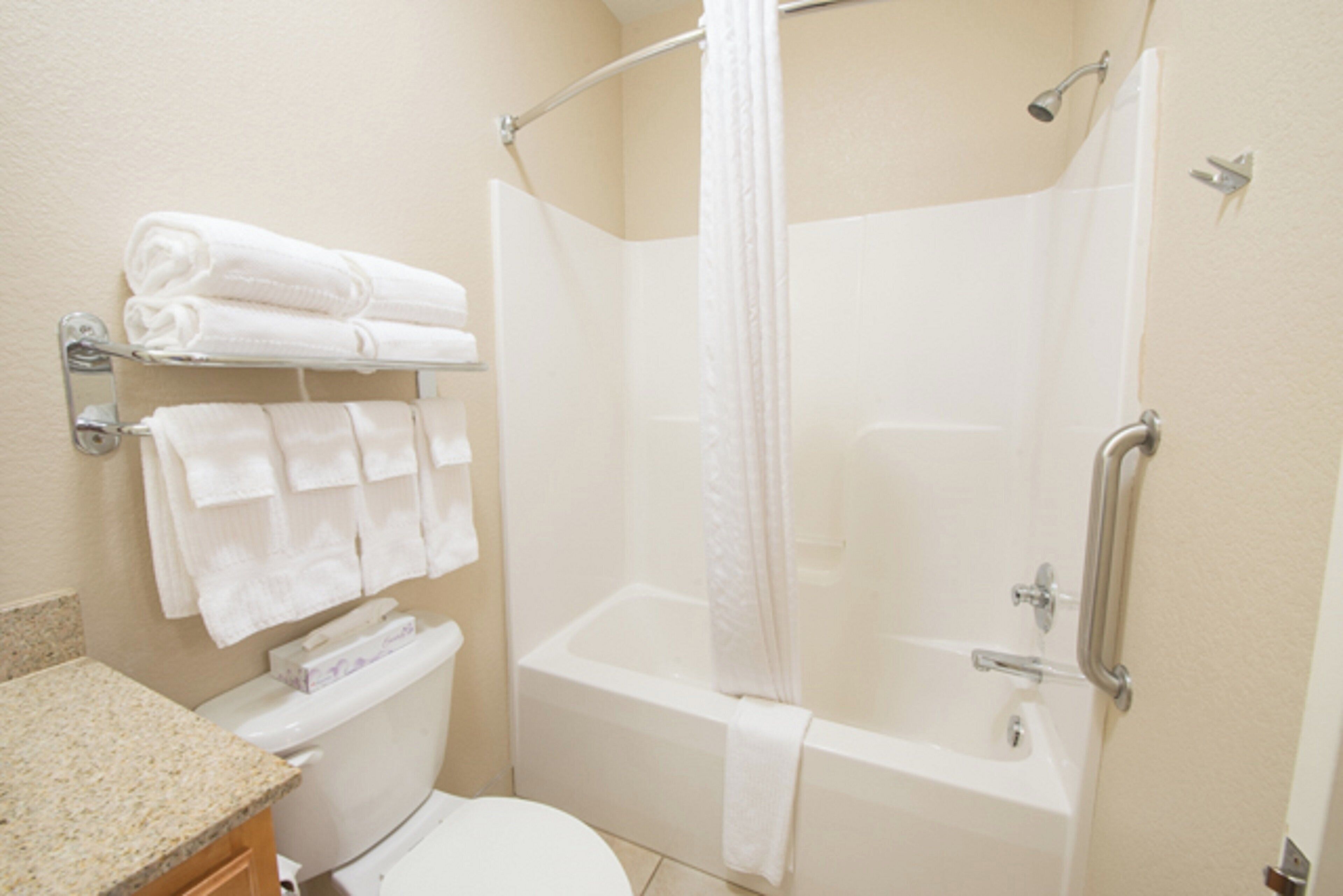 A bathroom with a toilet, a bathtub, a shower curtain, and a towel rack with folded towels.