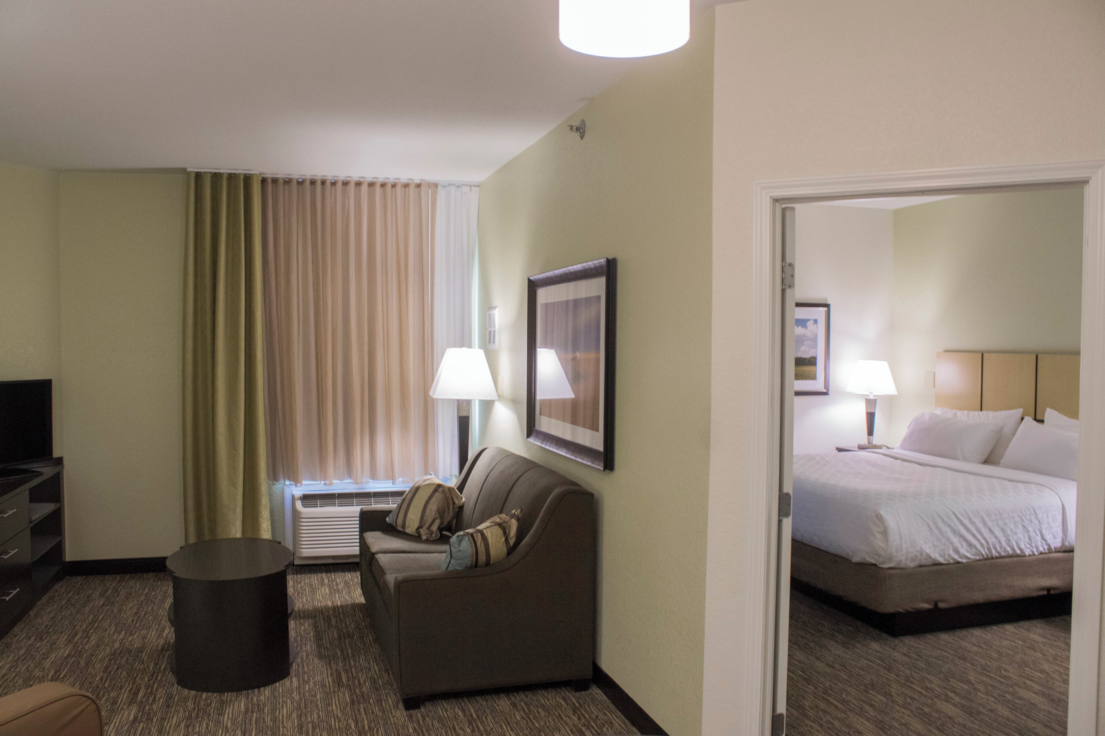 A hotel room with a sofa, a small table, a bed, and a television.