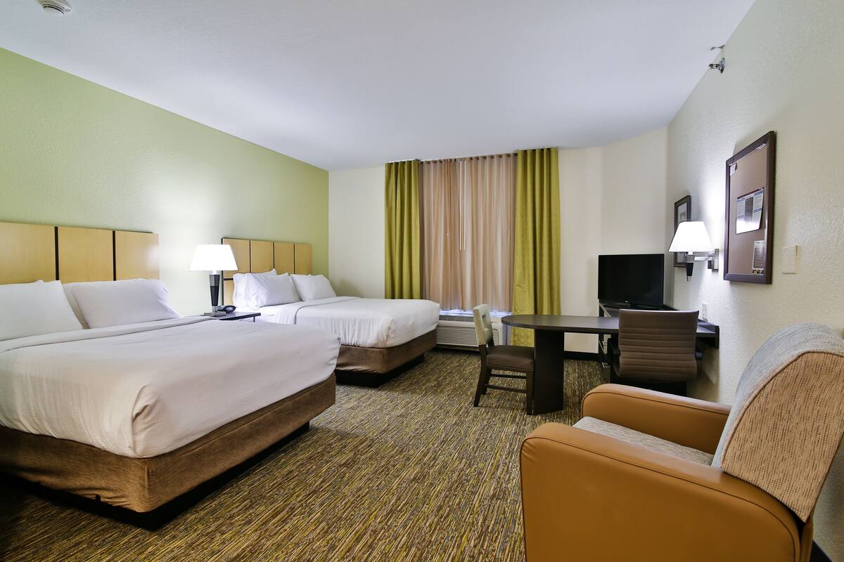 A hotel room with two beds, a desk, a chair, and a television.
