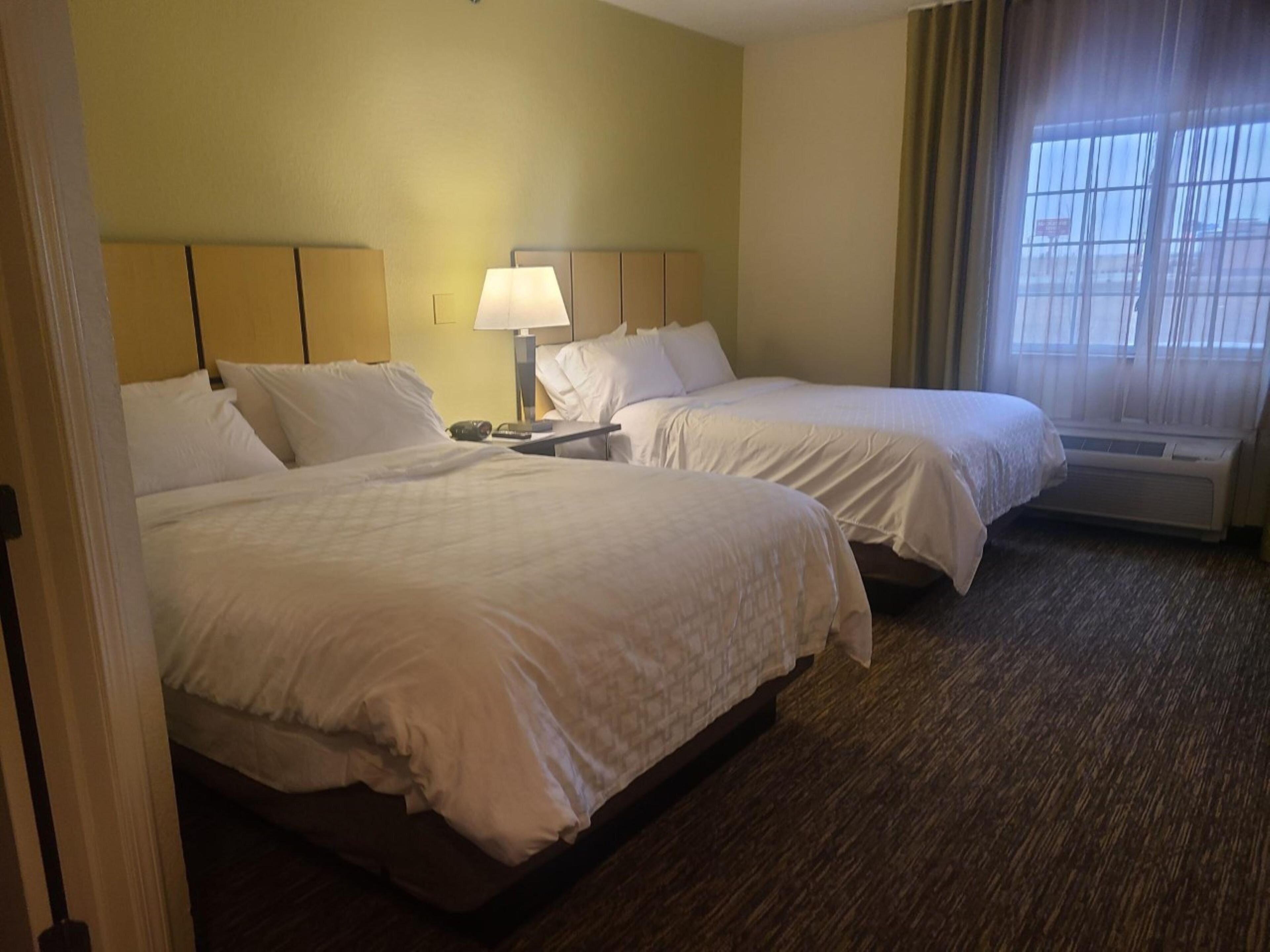 A hotel room with two beds, a nightstand, a lamp, and a window with curtains.