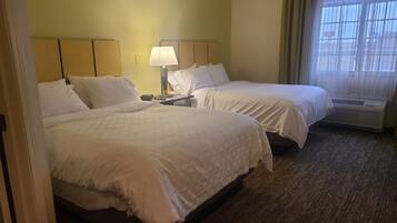 A hotel room with two beds, a nightstand, a lamp, and a window with curtains.