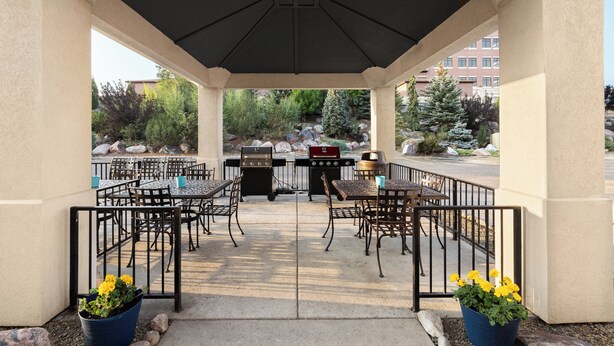 An outdoor patio with tables and chairs, a barbecue grill, and potted plants. - Candlewood Suites Bismarck by IHG (Bismarck)