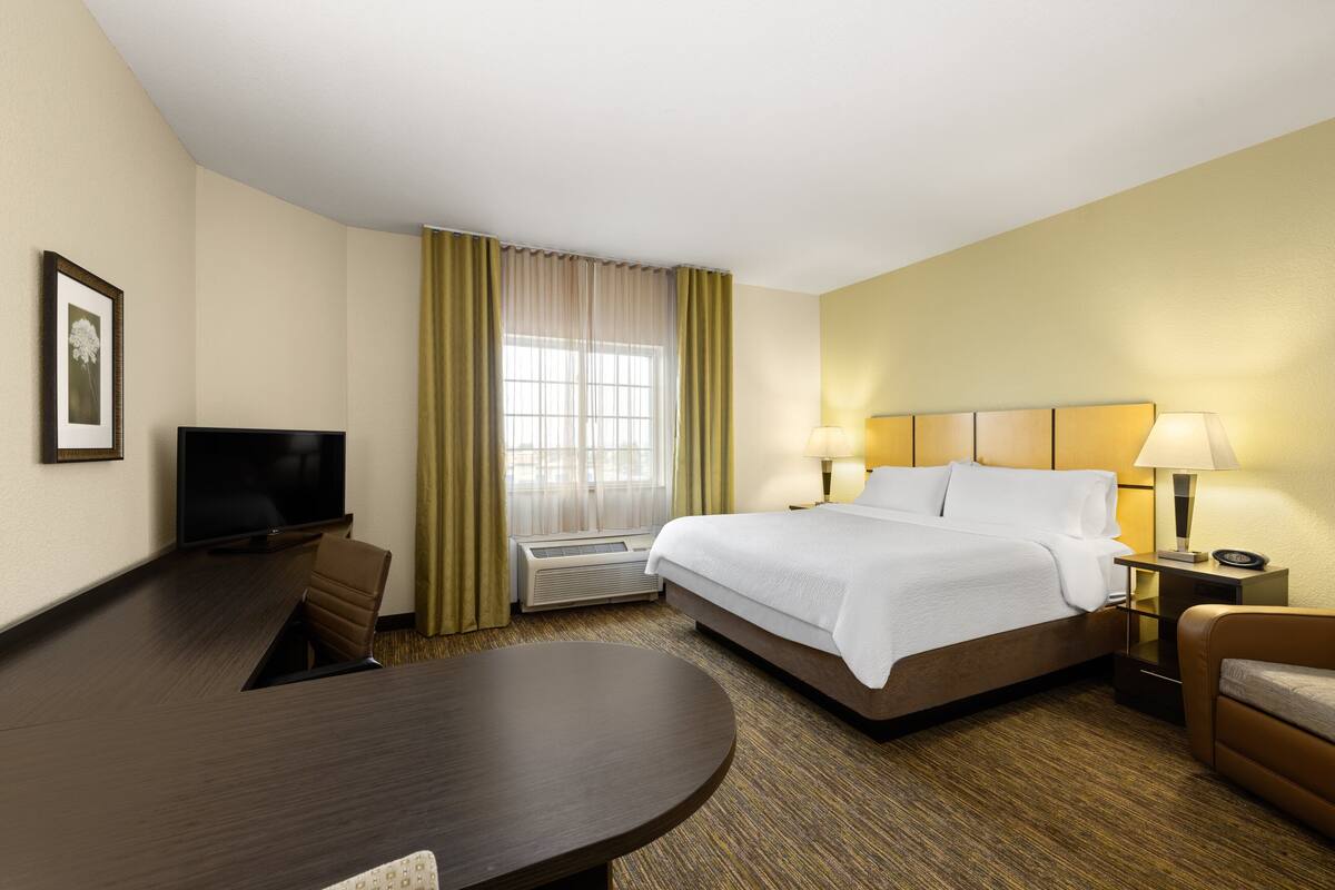 A hotel room with a bed, a desk, a television, and a window with curtains.