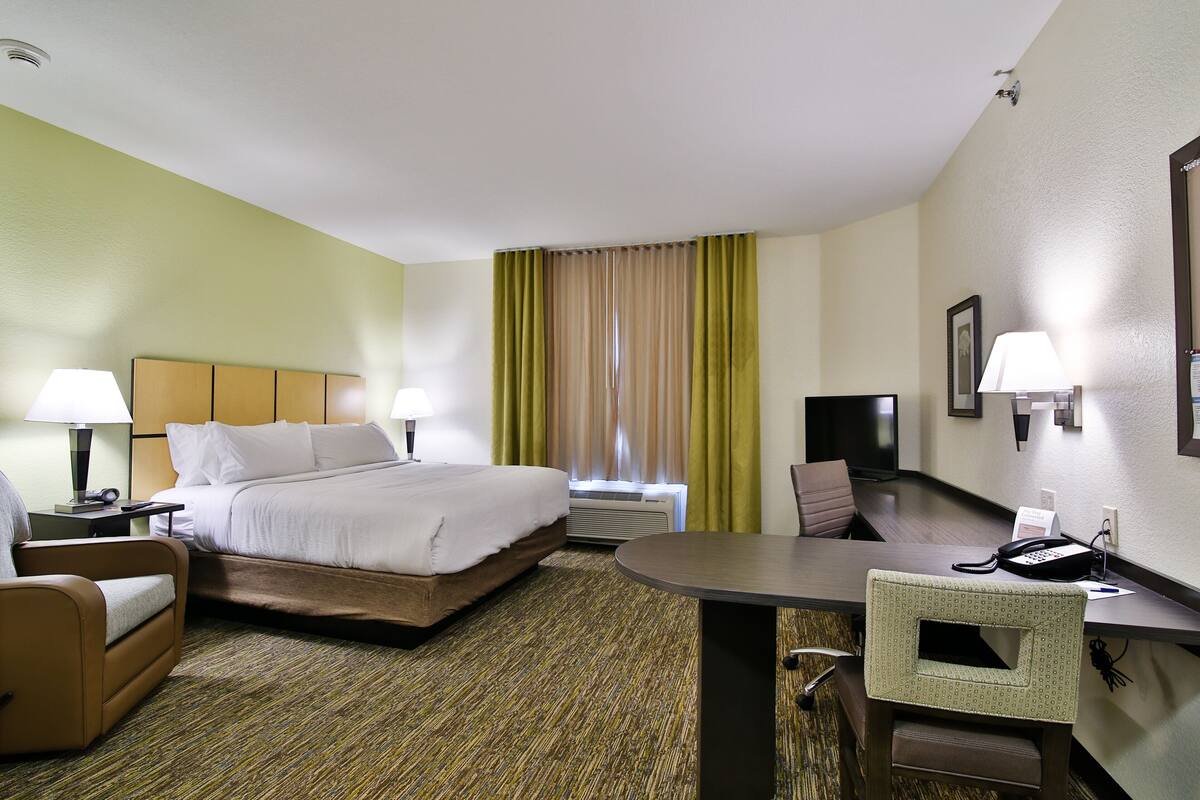 A hotel room with a bed, a desk, a chair, a lamp, and a telephone.
