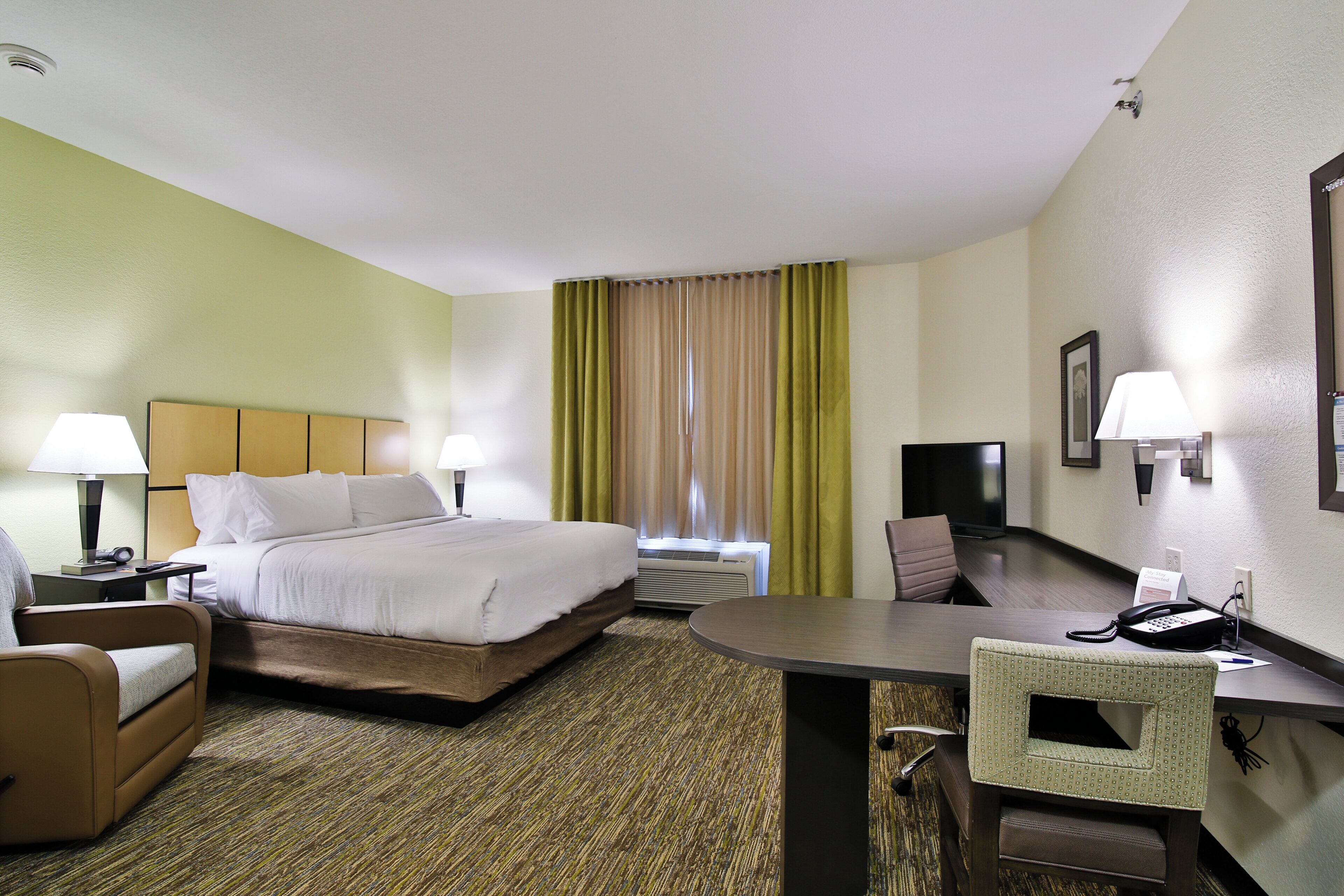 A hotel room with a bed, desk, chair, lamp, and a telephone.
