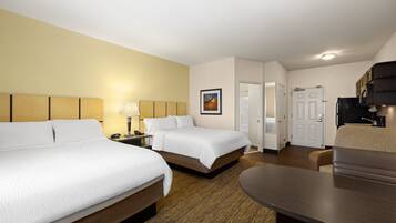 A hotel room with two beds, a desk, a chair, and a door leading to another room.