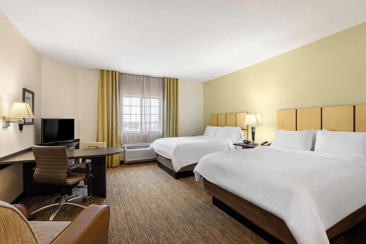 A hotel room with two beds, a desk with a computer, a chair, and a TV.