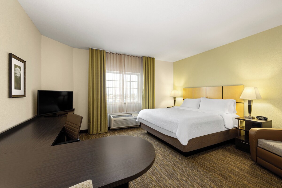 A hotel room with a bed, a desk, a television, and a window with curtains.