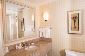 A bathroom with a granite countertop sink, a large mirror, a framed artwork, and a towel rack. - Hilton Garden Inn Erie (Erie)