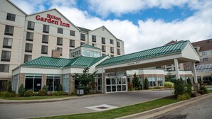 Un Hilton Garden Inn con cielo despejado, entrada techada y estacionamiento.