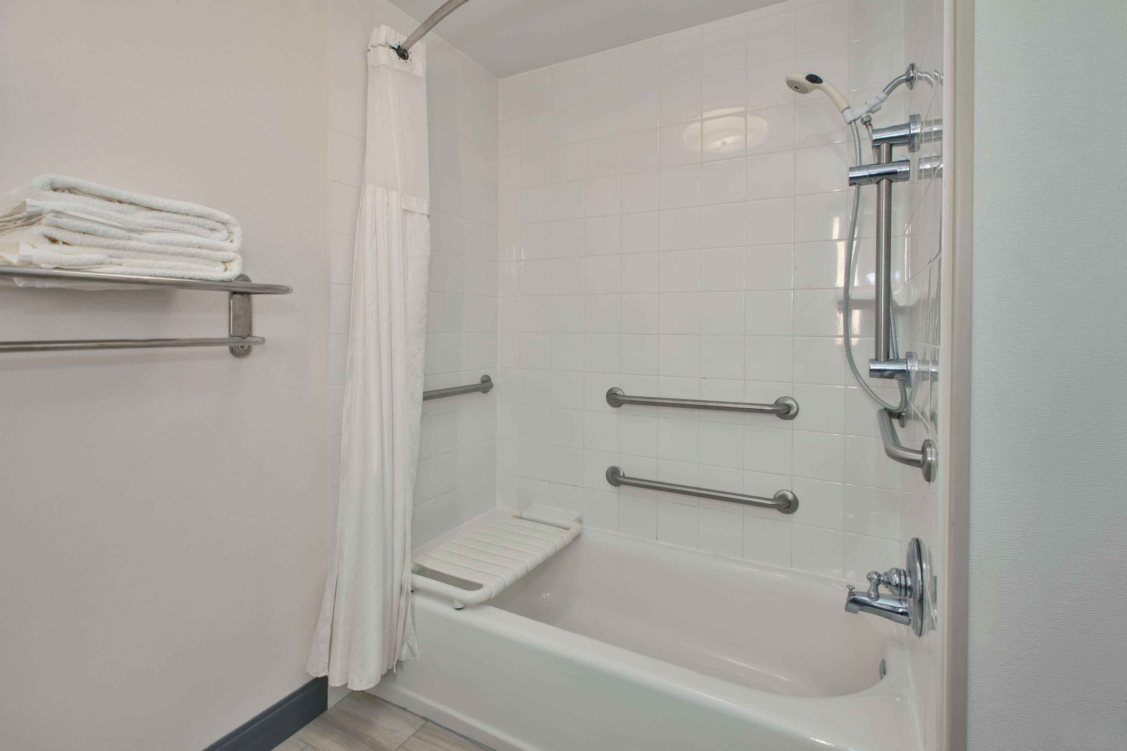 Une salle de bain blanche avec une baignoire, des barres d’appui et un porte-serviettes.