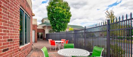 An outdoor patio with a brick wall, a round table, and green chairs.
