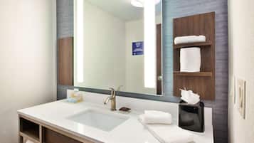 Une salle de bain d’hôtel avec un grand miroir, un lavabo, un porte-serviettes et un distributeur de savon.