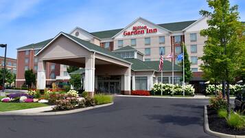 A Hilton Garden Inn with a covered entrance, landscaped gardens, and a clear blue sky.