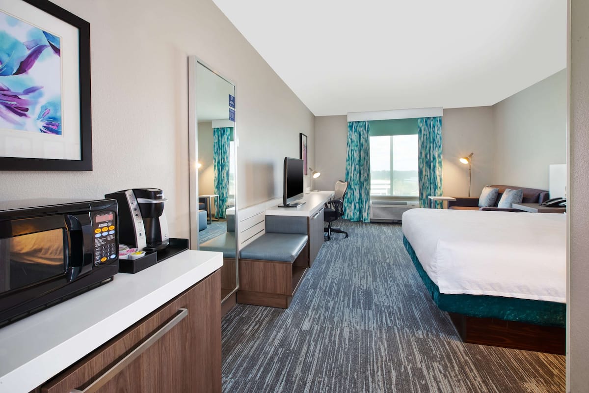 Een hotelkamer met een bed, bureau, magnetron en een groot raam met gordijnen.