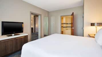Een hotelkamer met een bed, een televisie op een houten kast, een zichtbare badkamer door een geopende deur, en een bedlampje.