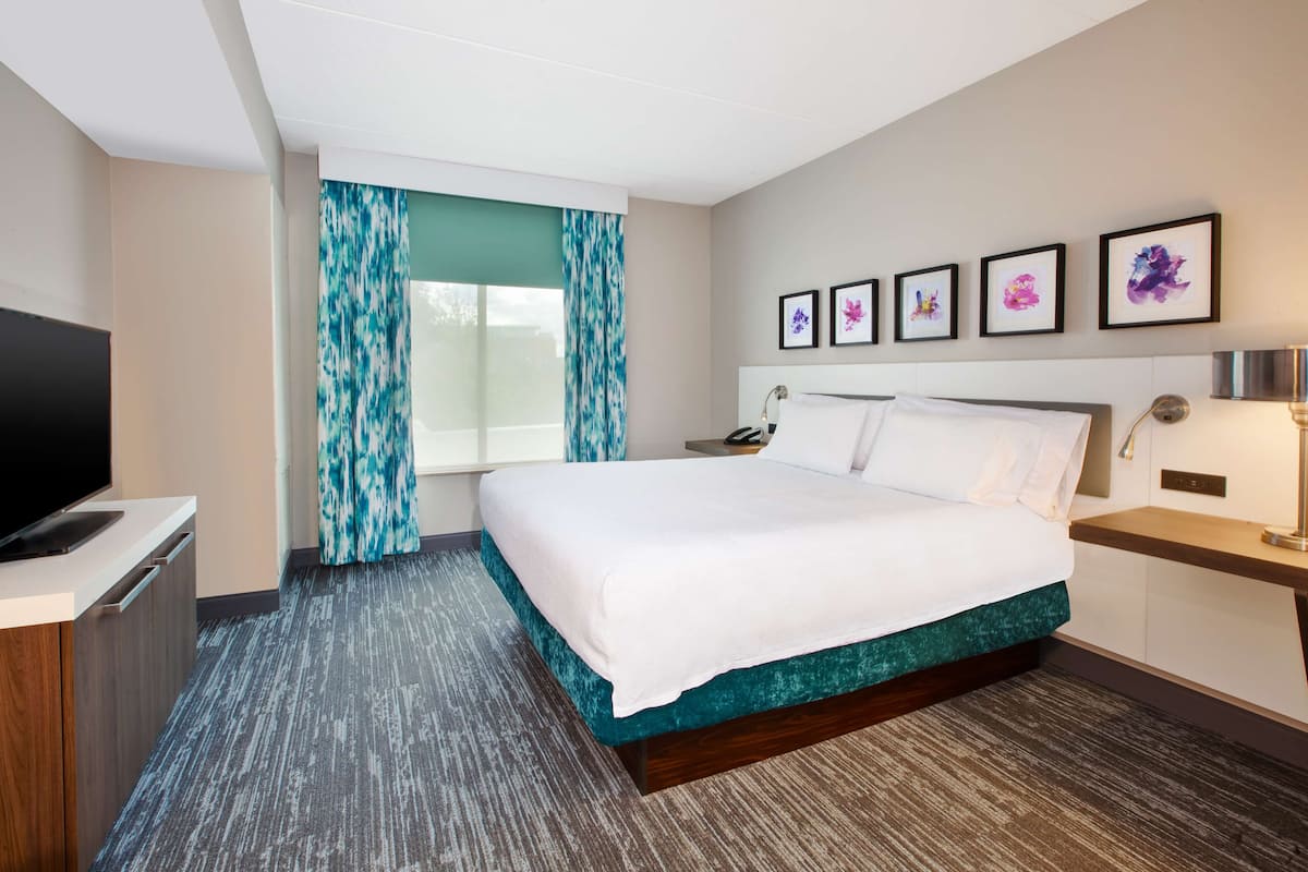 Een hotelkamer met een groot bed, een televisie, een bureau en een raam met gordijnen.