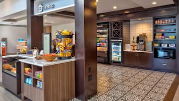 Un área de servicio de alimentos en un hotel, con un mostrador de autoservicio, bebidas refrigeradas y un microondas.