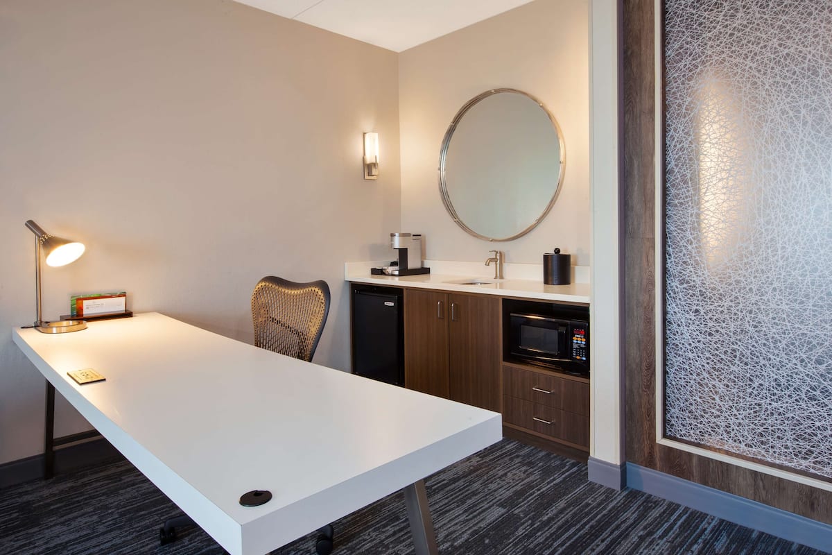 Een moderne hotelkamer met een wit bureau, een ronde spiegel, een koffiezetapparaat en een magnetron.