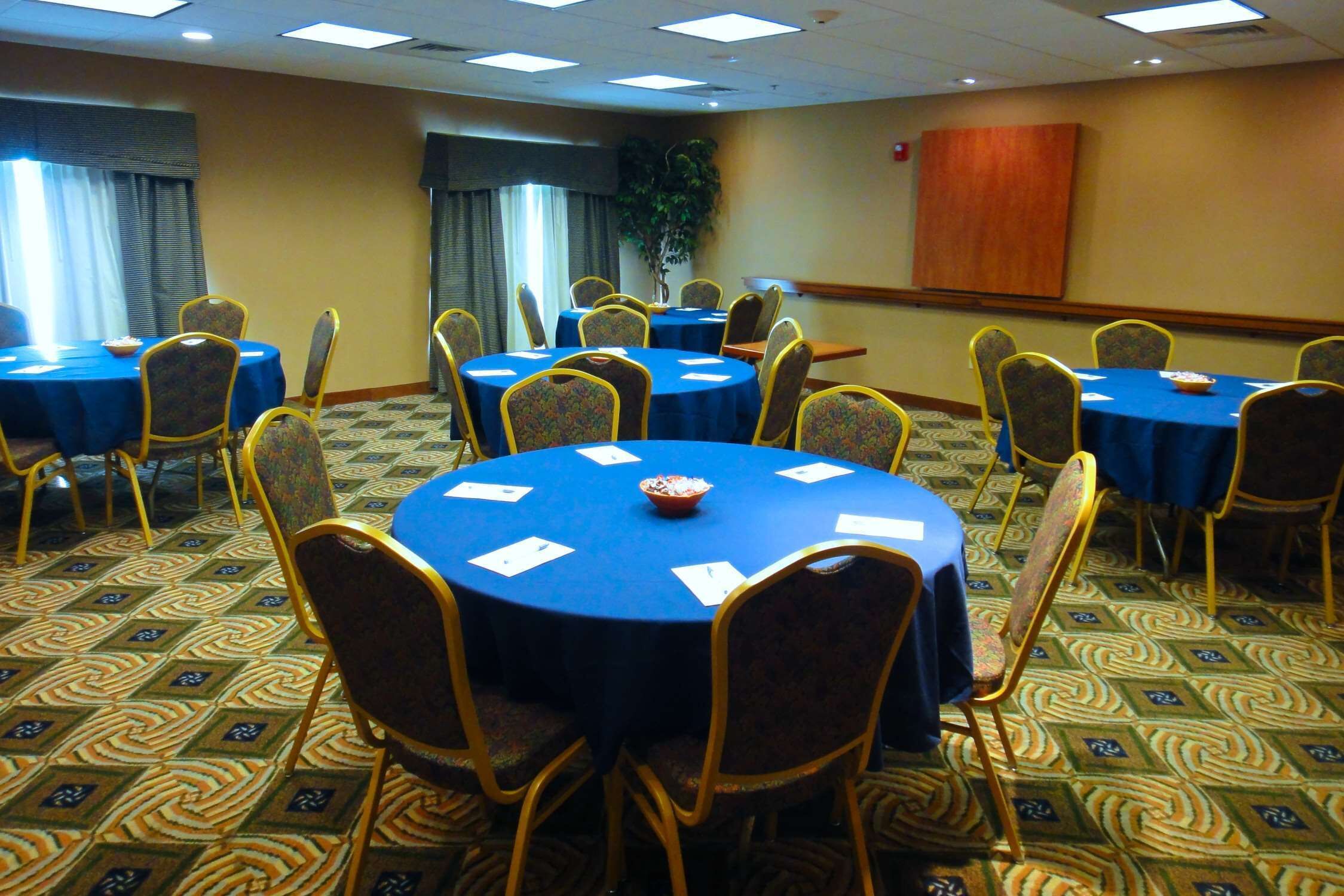 A conference room with multiple round tables, each with a blue tablecloth and matching chairs.