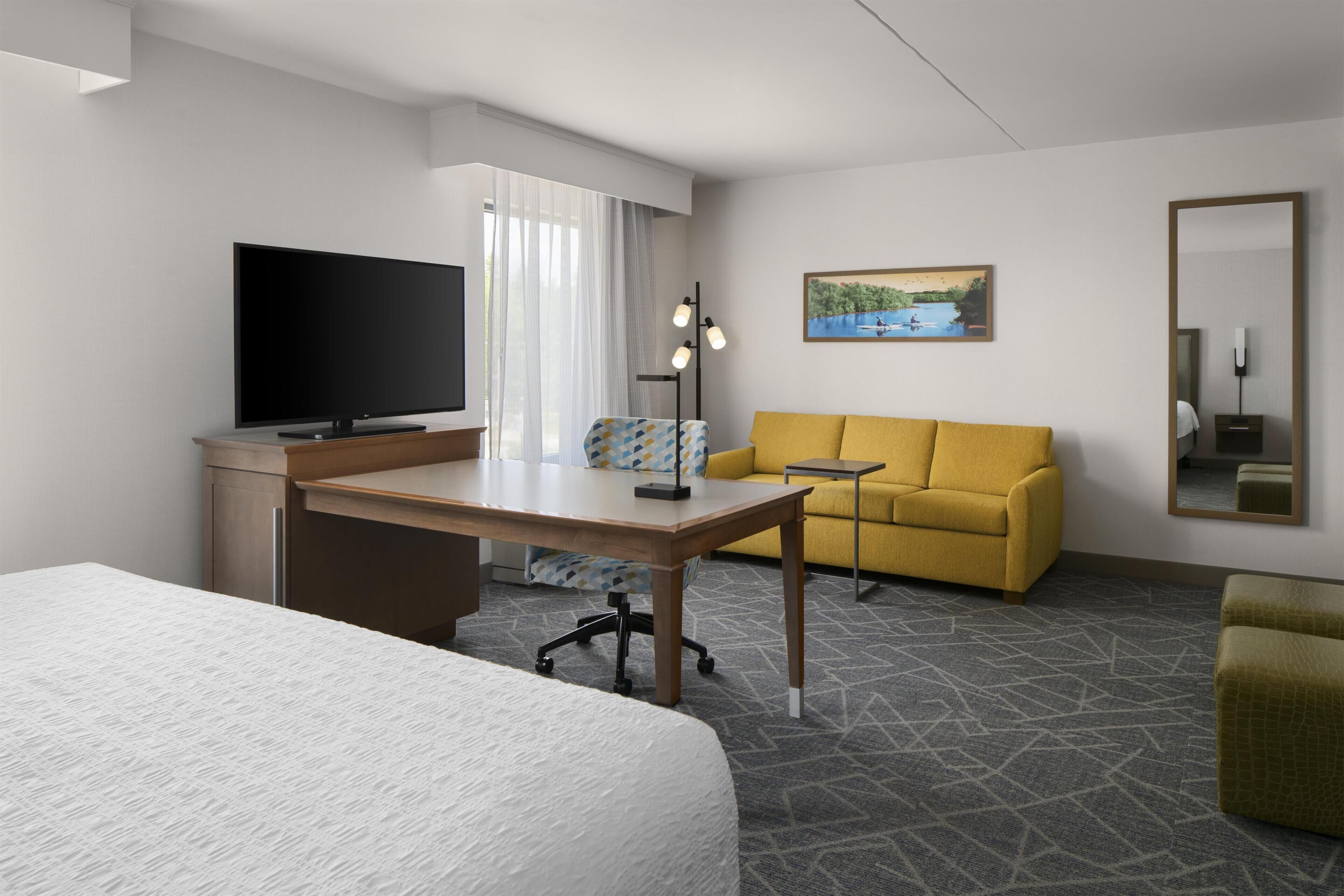 Habitación de hotel con cama, escritorio y silla, sofá, televisión y un cuadro en la pared.