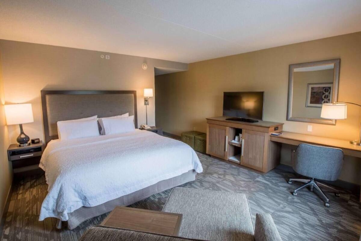 A hotel room with a large bed, a desk, a chair, a TV, and a mirror.