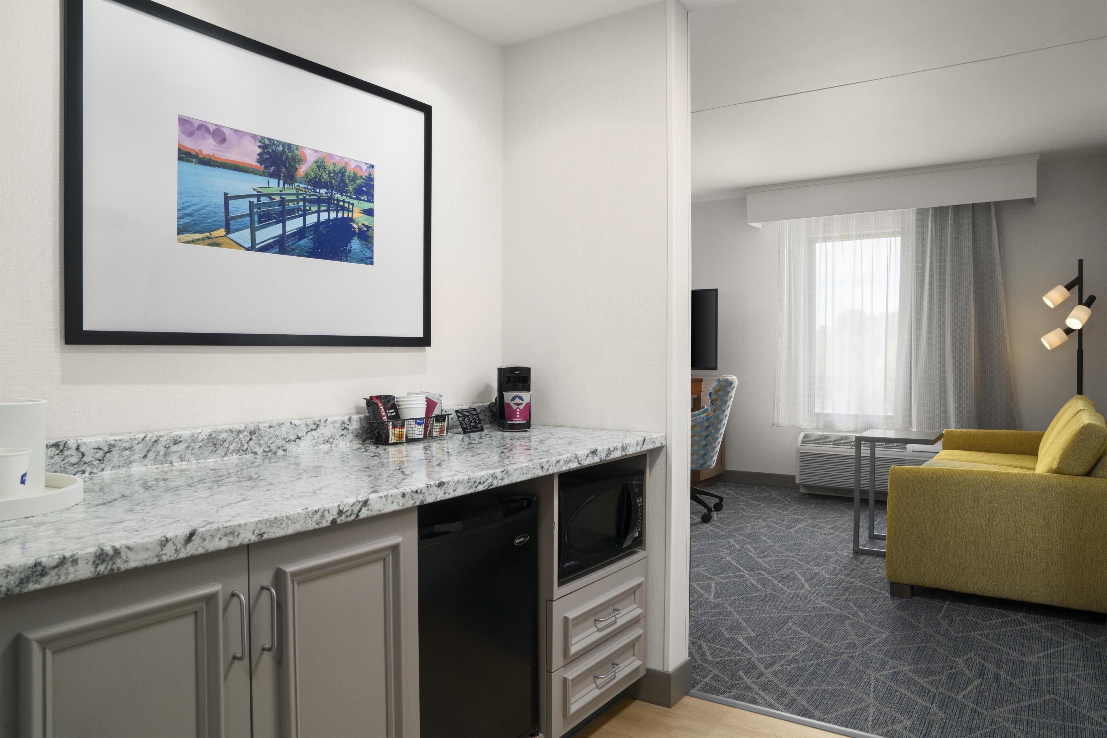 A hotel room with a marble countertop, a television, a sofa, a chair, and a framed picture on the wall.