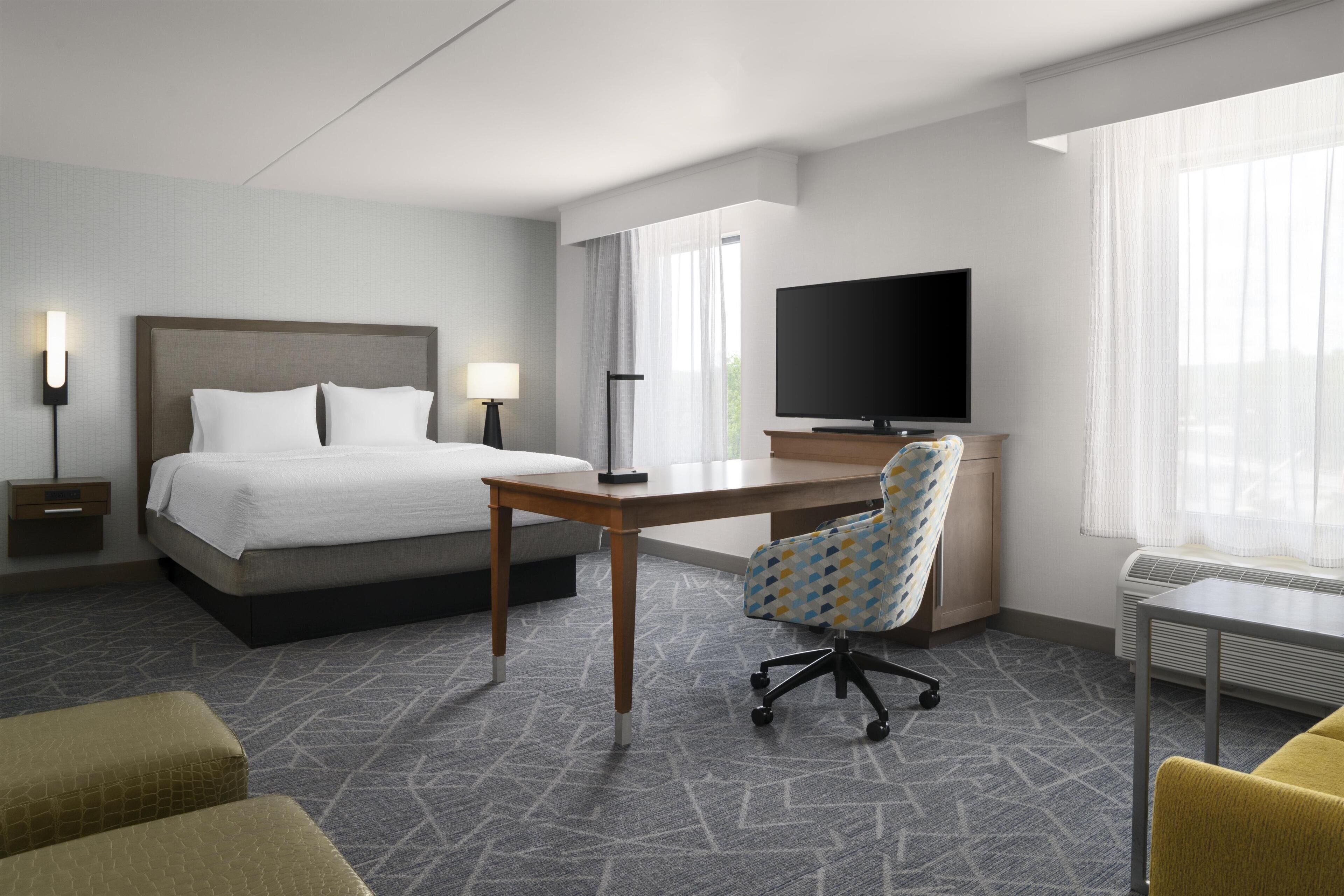 A hotel room with a bed, desk, chair, television, and a window.