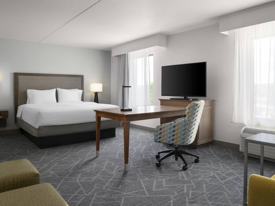 A hotel room with a bed, desk, chair, television, and a window.