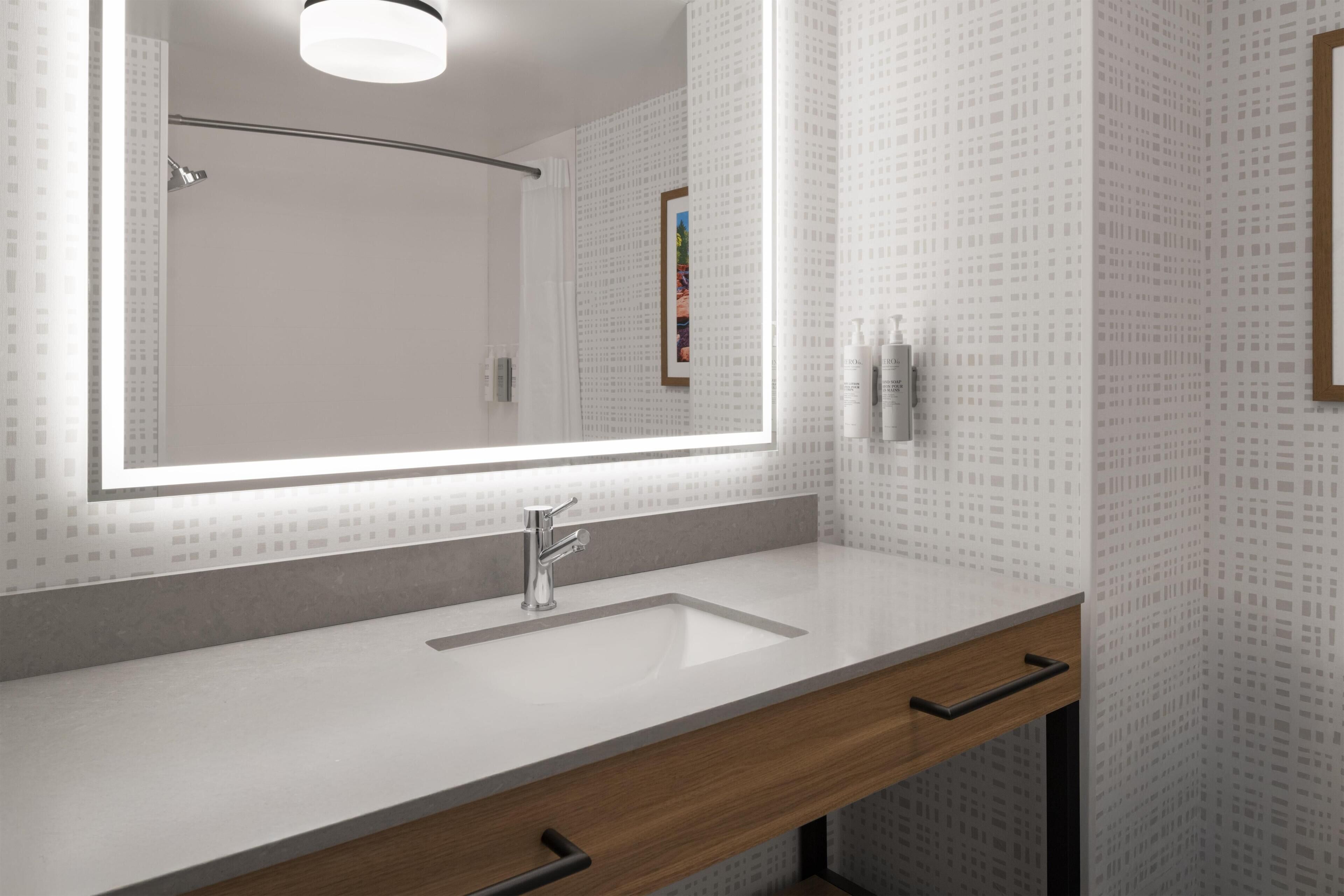 Un baño moderno con un espejo grande, un lavamanos y un perchero para toallas.
