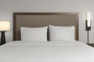 Una cama con cabecera, dos almohadas, una lámpara de noche y una lámpara de pared.