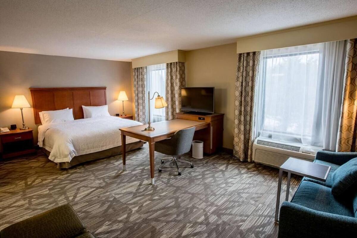 A hotel room with a bed, desk, TV, and seating area.